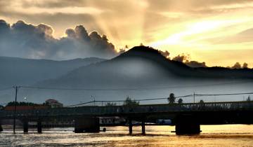 Sunset over a mountain range with a bridge and river in the foreground.