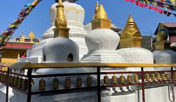 White and gold stupa surrounded by prayer wheels and flags.