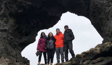 Group of four posing under a rock arch with a cloudy sky.