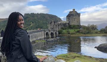 Woman posing in front of a castle by a scenic loch.