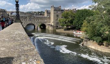 Bridge over a weir in a river with old buildings in the background.