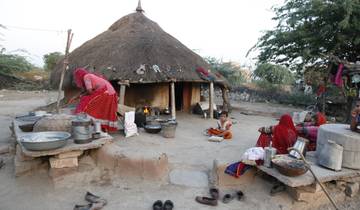 Rural scene with a traditional hut, women cooking outdoors and a child sitting.