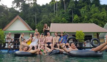 Group of people sitting on a floating platform with houses behind.