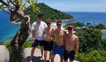 Four men posing on a rock with a beach view.