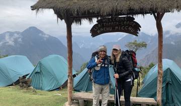 Two hikers at a lodge with mountains and tents.