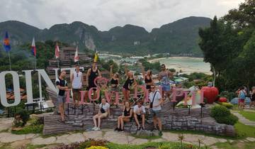 Group in front of 'I Love Phi Phi' sign with beach and mountains.