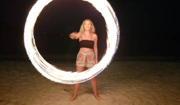 Woman spinning a fire hoop on a beach at night