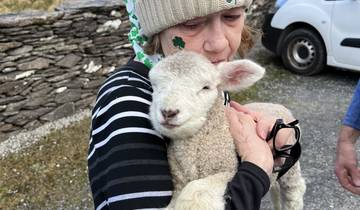Woman hugging a lamb with a scenic backdrop.