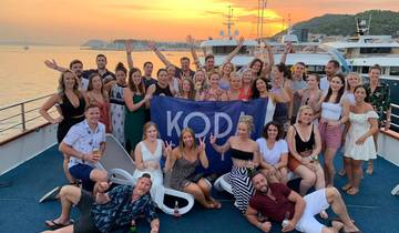 Large group celebrating on a boat at sunset with a banner.