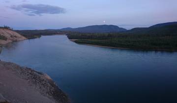 River landscape at dusk with a distant moon and mountains.