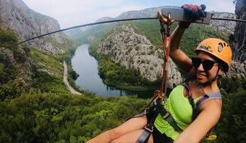 Person zip-lining over a scenic river and rocky landscape.