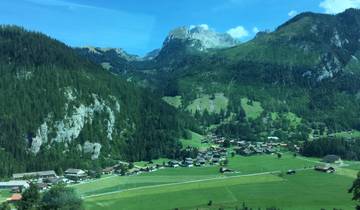 Villages and pastures in a lush green valley beneath mountains.