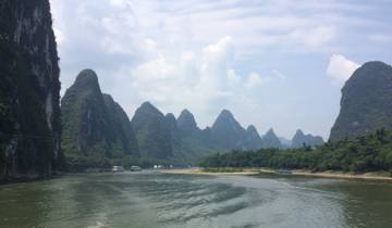 River surrounded by karst mountains under a cloudy sky.