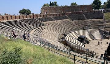 Ancient Roman theater with stone seating and tourists visiting.