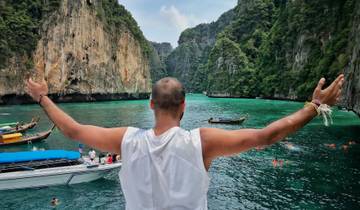 Person with arms raised on a boat in a tropical bay with limestone cliffs.