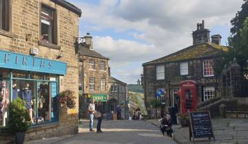 A street scene in a quaint town with stone buildings, shops, and a red phone booth.