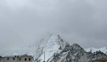 Camp at the base of a snowy mountain with clouds overhead.
