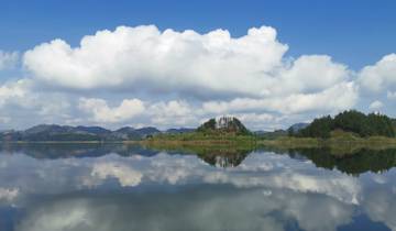 A reflective lake with clouds and lush surroundings.
