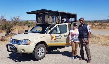 Couple posing in front of a safari vehicle in a dry landscape.