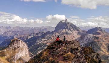 Two people sitting on a rocky peak enjoying mountain views.