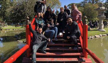 Group of people posing on a red bridge over a pond in a park.
