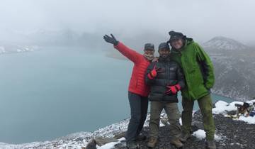 Three people posing by a lake in a mountainous area.