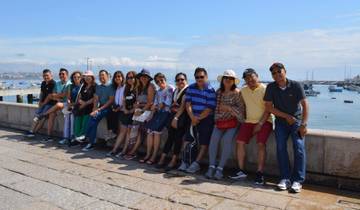 People sitting on a seaside wall with boats in the background.