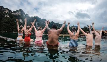 Friends sitting in the water with hands raised in celebration.