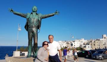 Couple posing with a large statue in a coastal town.