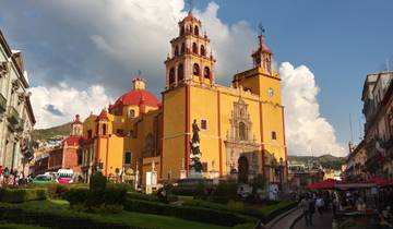A brightly colored cathedral with a garden and cloudy sky.