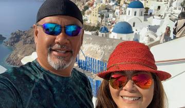 Couple smiling with the iconic blue domes of Santorini in the background.