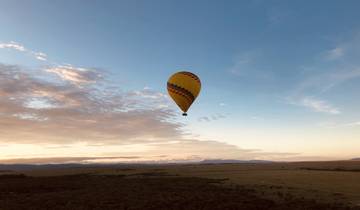 Hot air balloon floating over a scenic plain at sunset.