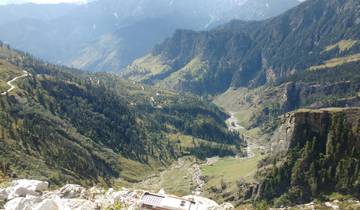Panoramic view of a deep valley with roads and trees, mountains in the background.