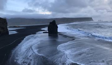 Black sand beach with sea stacks and waves.