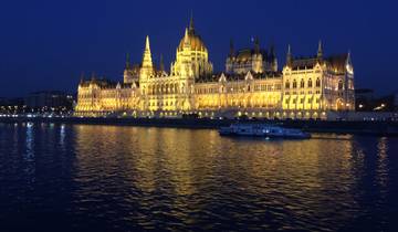 Night view of the illuminated Budapest Parliament Building across a river.