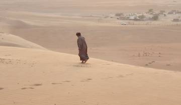 A person walking barefoot across sand dunes with scattered settlements.