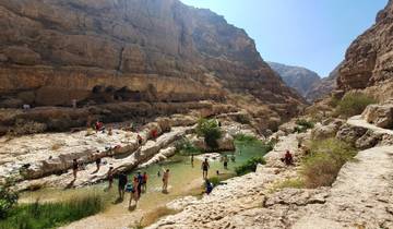 A crowded natural limestone canyon pool with people swimming.