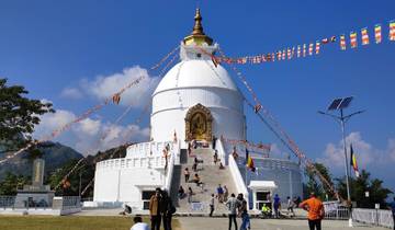 People climbing steps of a large white stupa with flags and blue sky.