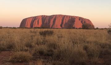 View of Uluru rock formation in a field during sunset.