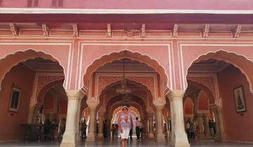 Woman standing in front of pink arched corridors with intricate designs.