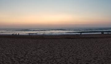 Sunset over a calm beach with people silhouetted.
