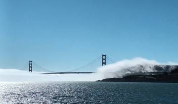 Golden Gate Bridge partially obscured by fog over a sparkling body of water.