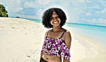 Happy person posing on a white sandy beach with ocean in the background.