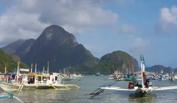 Boat-filled port with towering rock formations.