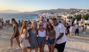 Group posing on a picturesque beach with white buildings in the background.