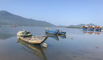 Serene lake with boats and wooden huts, surrounded by mountains.