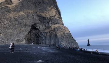 A black sand beach with basalt columns and people exploring.