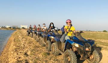 Group of people riding ATVs along a dirt path near a water body.