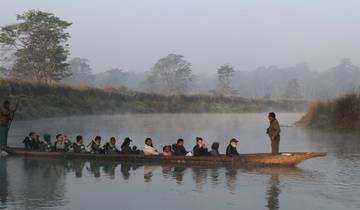Group of people on a canoe navigating a calm river surrounded by misty forest.