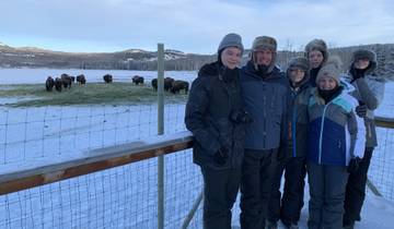 A family group standing by a fence, with bison in the snowy background.